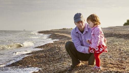 A father crouched down beside his daughter on the shoreline at Dunwich Beach